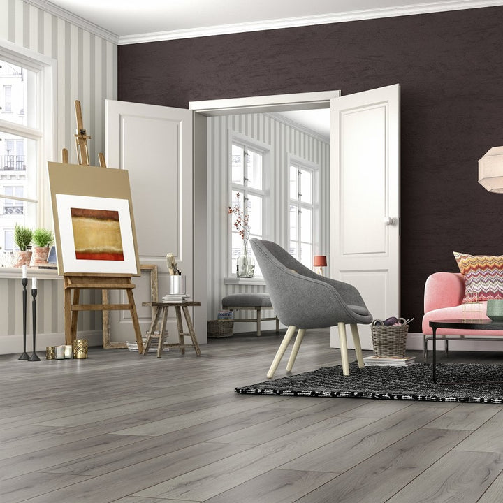 Modern living room with gray chair, pink sofa, artwork on an easel and Kronotex Superior Standard Plus Century Oak Grey D4175 7mm Laminate Flooring
